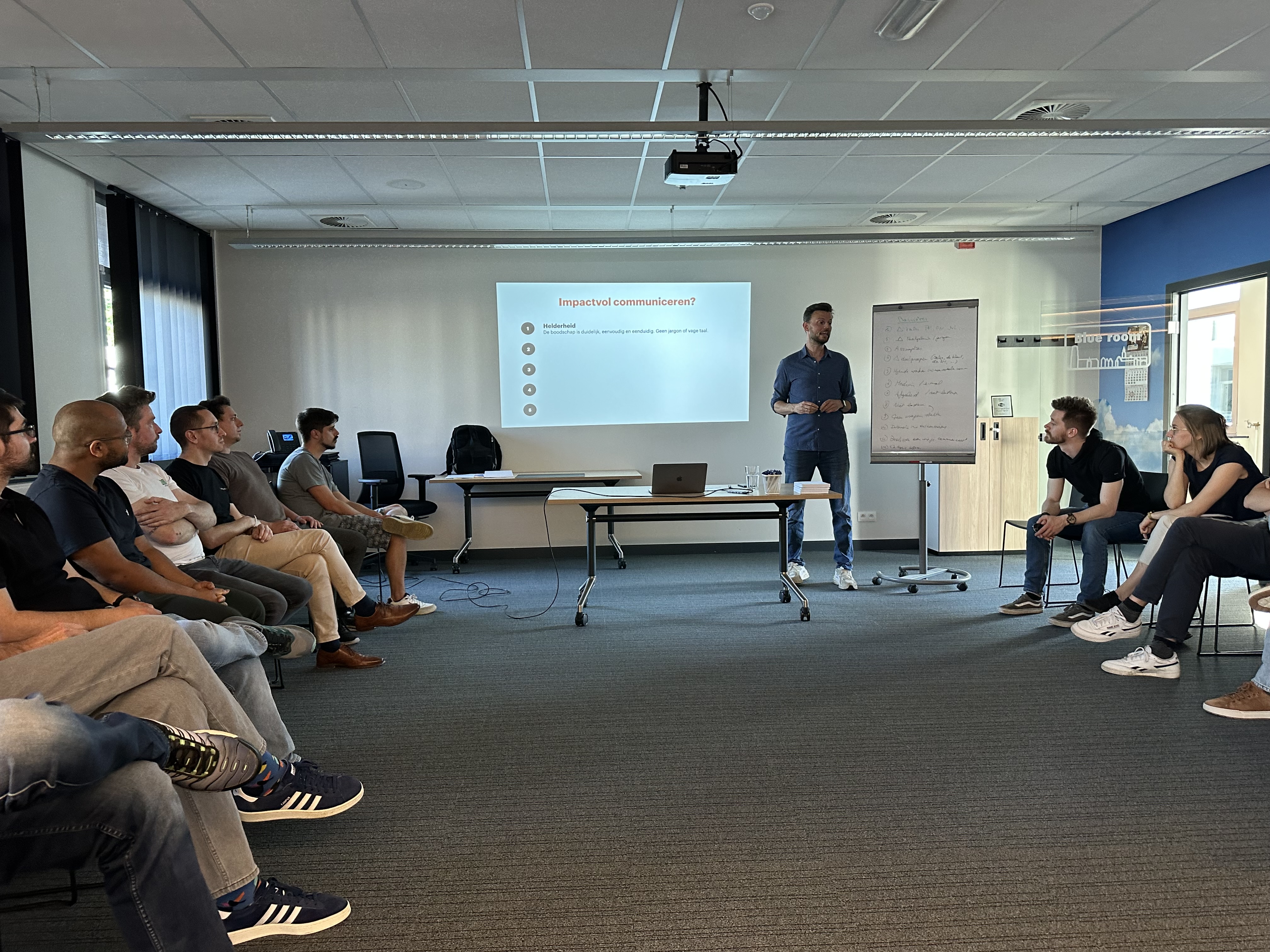 The trainer leading a discussion on **impactvol communiceren** (communicating with impact), providing practical tools for **navigating resistance** and improving project communication skills among professionals.