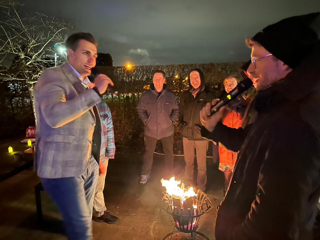 Colleagues together for a festive outdoor celebration, featuring warm drinks, a crackling fire, and joyful holiday vibes.