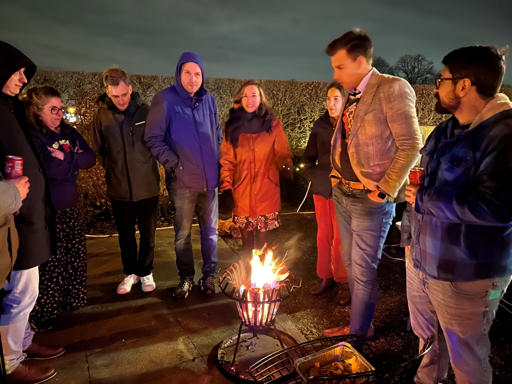 Itenium colleagues around a warm fire, enjoying festive drinks, good company, and the holiday spirit under the winter night sky.