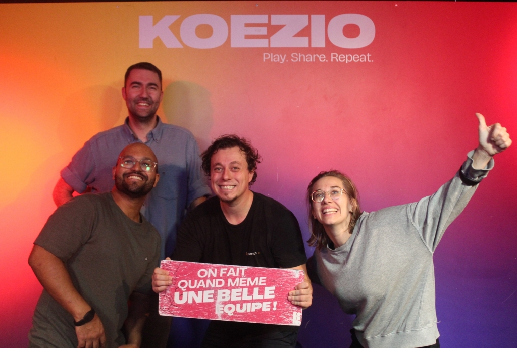 A group celebrating their successful **Koezio challenge** with a sign affirming their status as a great team, emphasizing **strong team collaboration** and successful **puzzle solving** at the event.