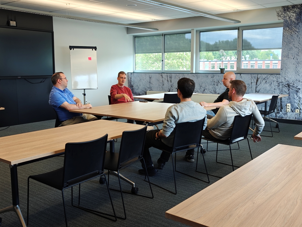 Itenium team members enjoying a relaxed, yet engaging, discussion during an Open Space Day, fostering informal knowledge sharing and strong team connections. This reflects a vibrant developer community.