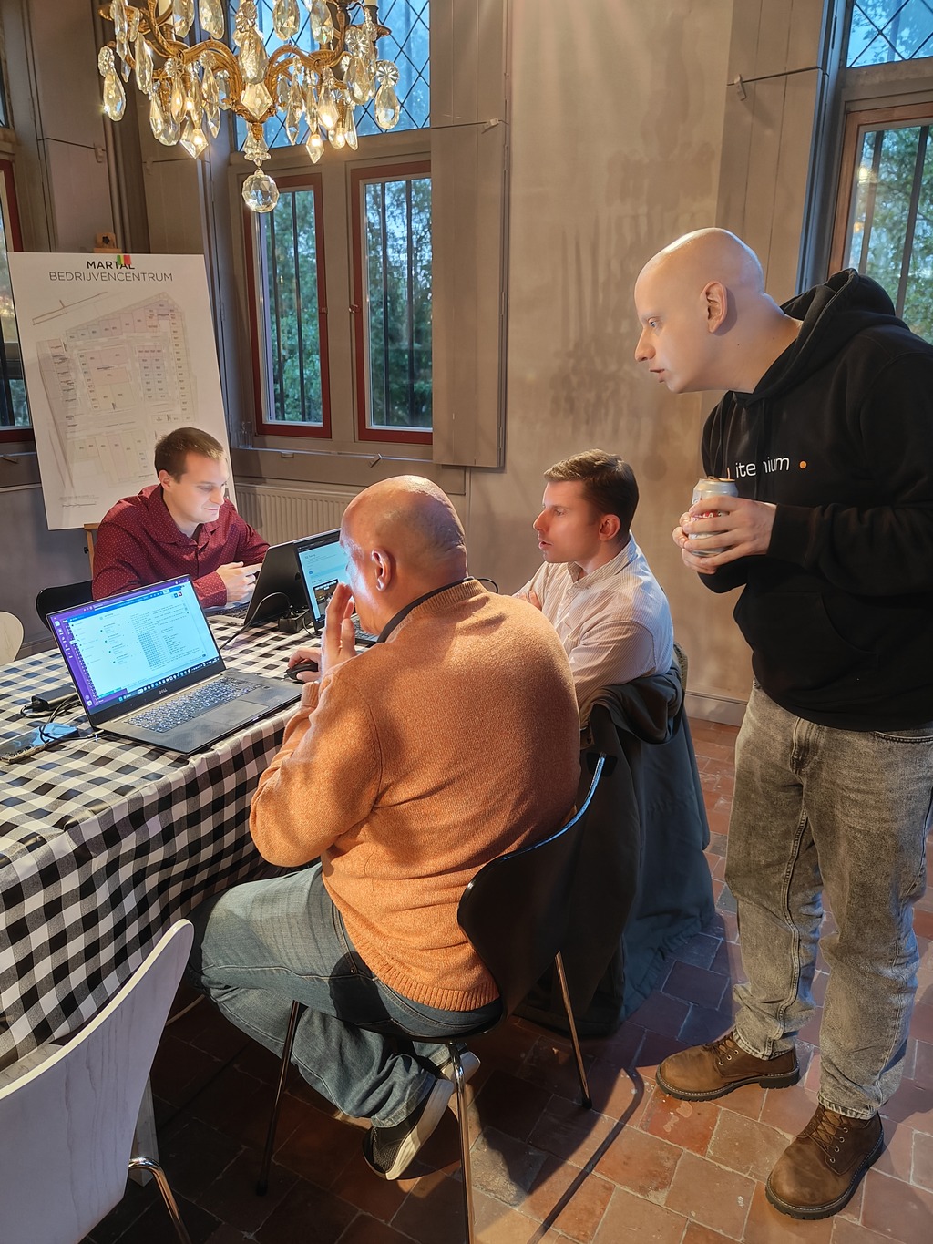 The developers intensely collaborating around a checkered table, focused on laptops in a warm, tech-driven environment, embodying the essence of teamwork, agile development, and real-time problem-solving.